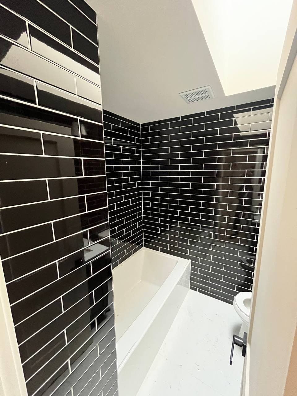 Tub surround in glossy black subway tile with a skylight above