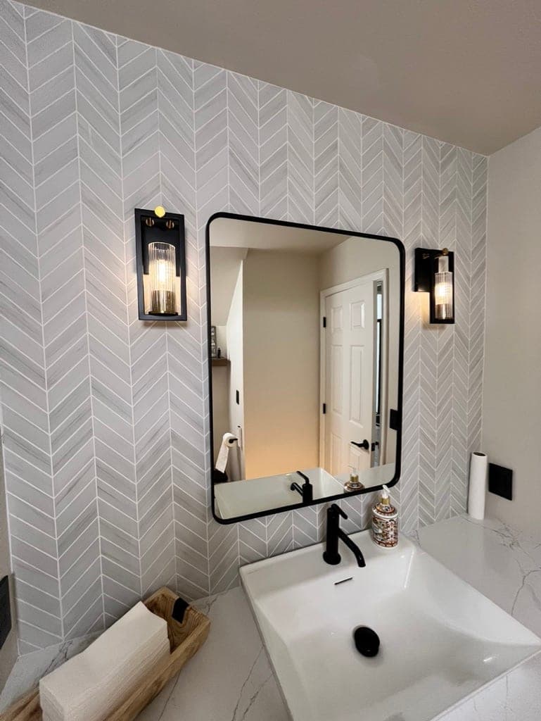 Close view of the black-framed mirror and sconces on the gray chevron wall