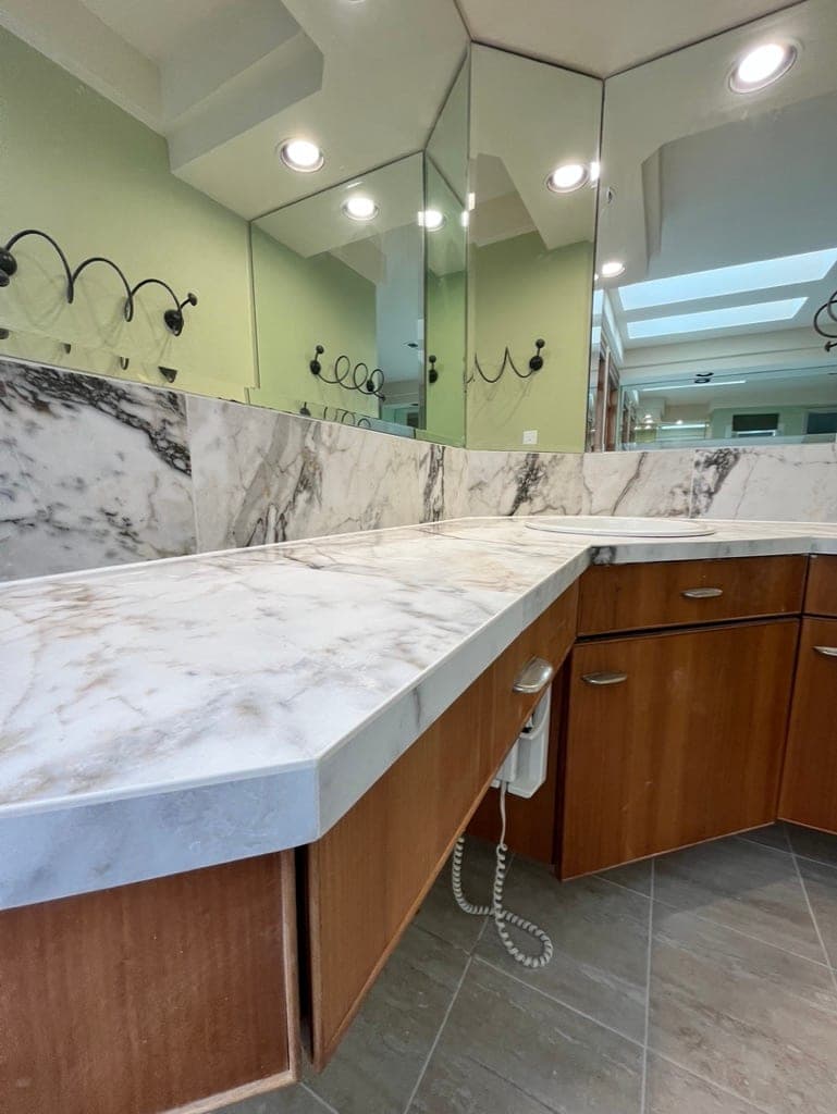 Slab counter and backsplash along the wood vanity with the gray tile floor