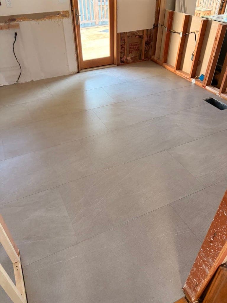 Gray large-format floor running toward a door to the deck, before grout