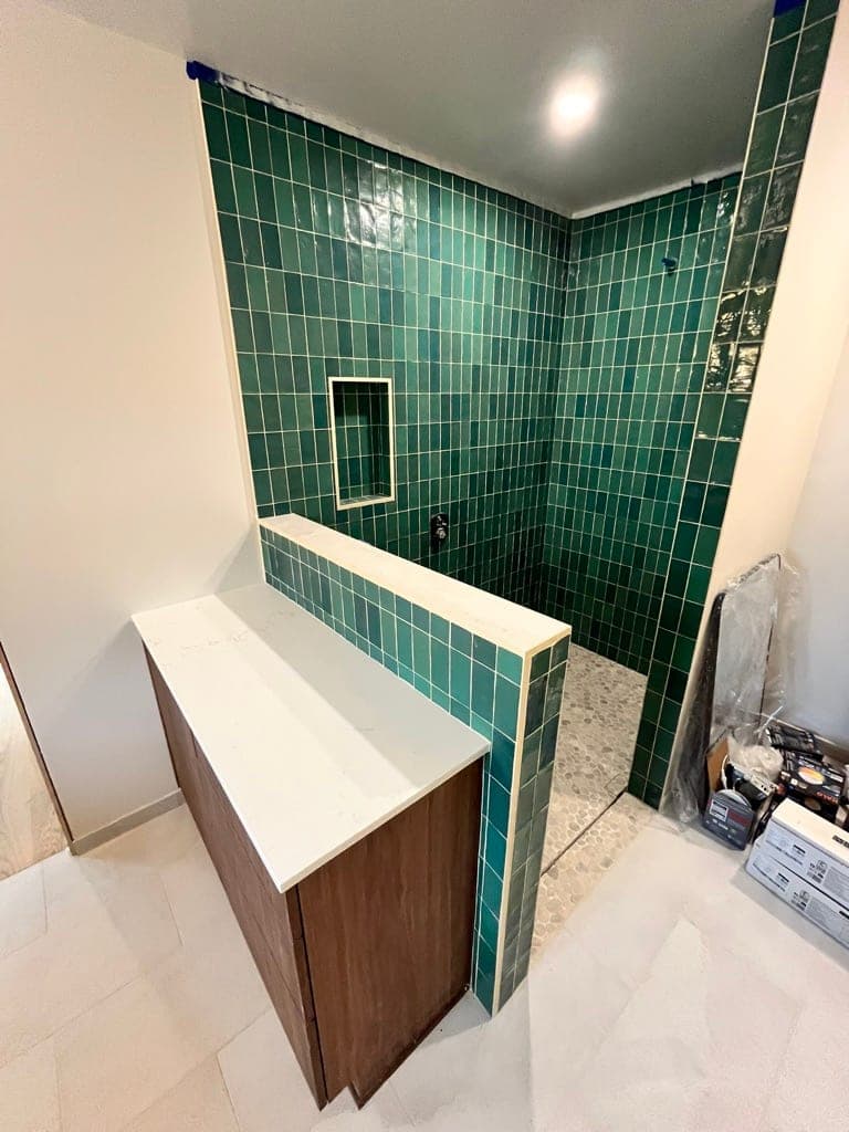 Green tile shower and half wall mid-install with the wood vanity in place