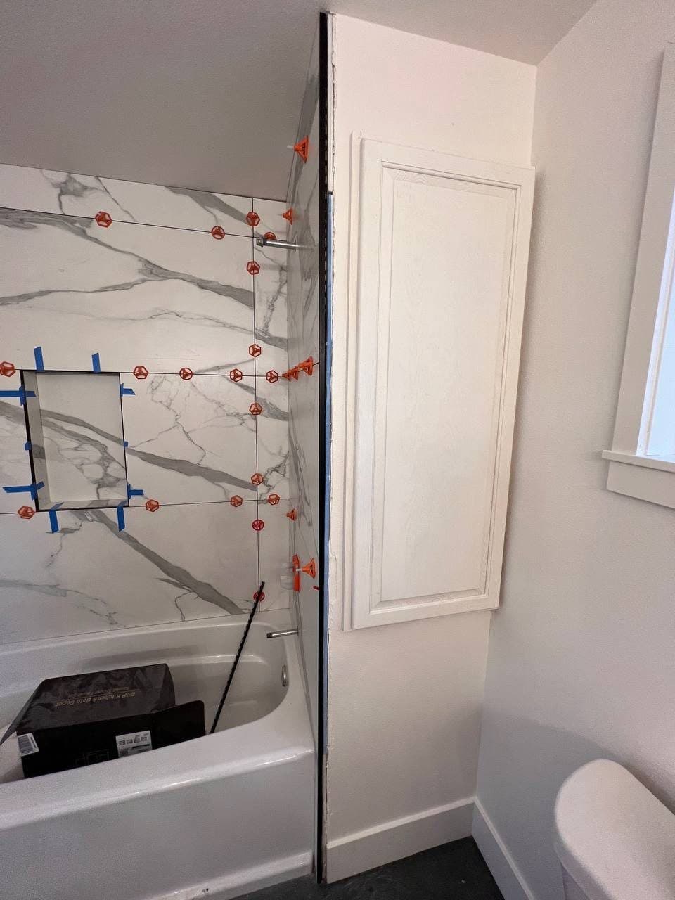 Marble-look porcelain wall tile mid-install with red leveling clips on every joint
