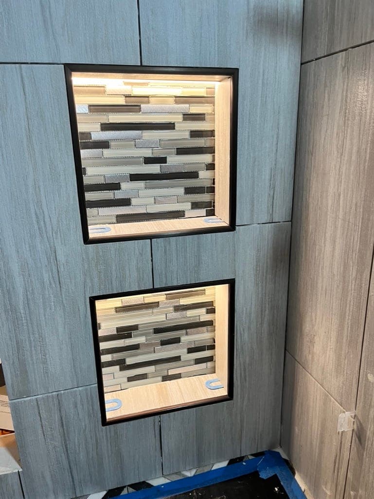 Two recessed niches lined with glass mosaic in a gray wood-look tile wall
