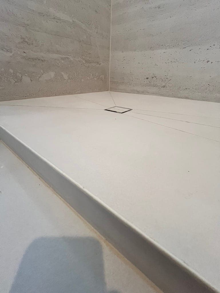 Stone-look shower pan pitched to a center drain with the curb set
