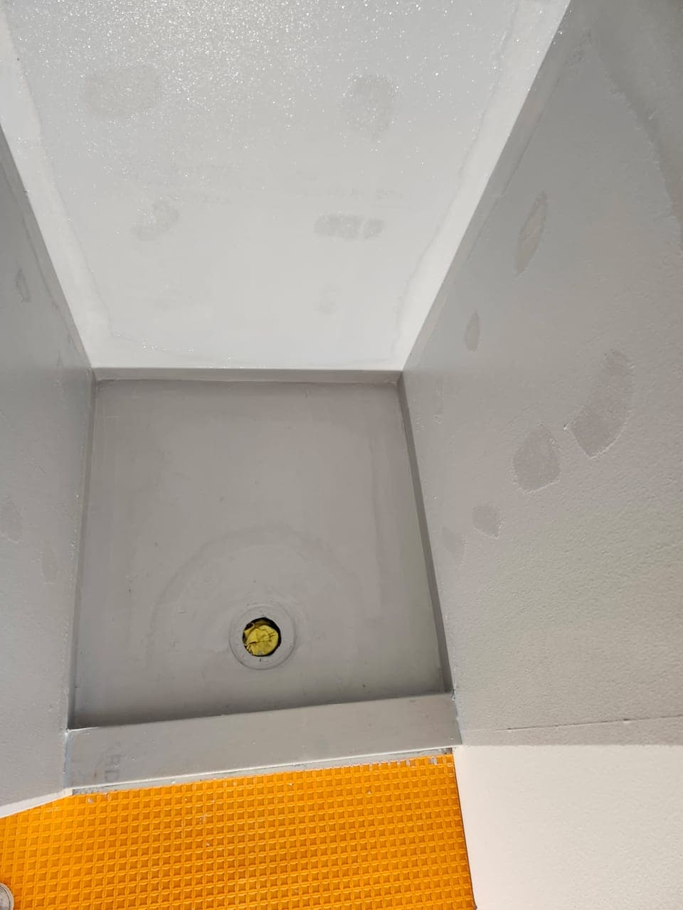 Shower pan and walls coated in gray liquid waterproofing with the drain set