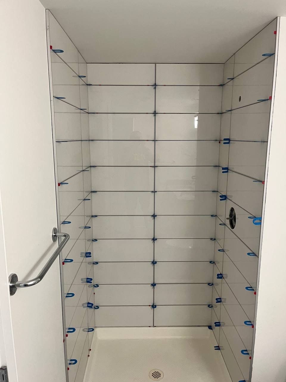 Shower walls mid-install in white large-format tile with blue leveling clips