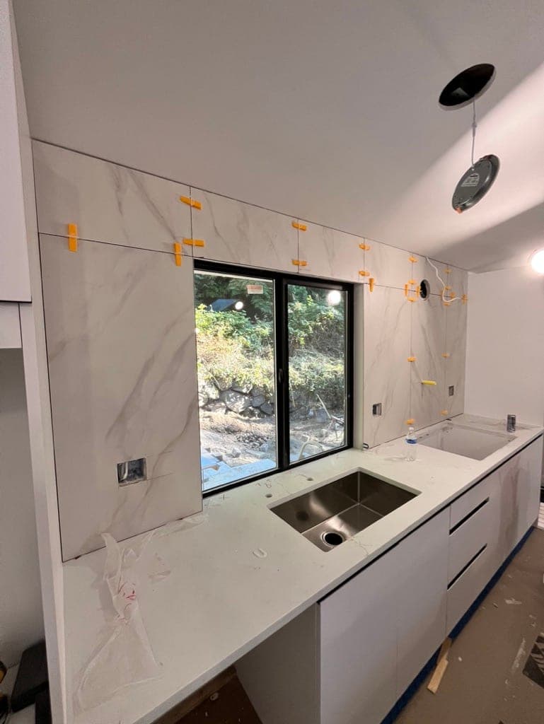Slab backsplash panels mid-install around the kitchen window with leveling clips
