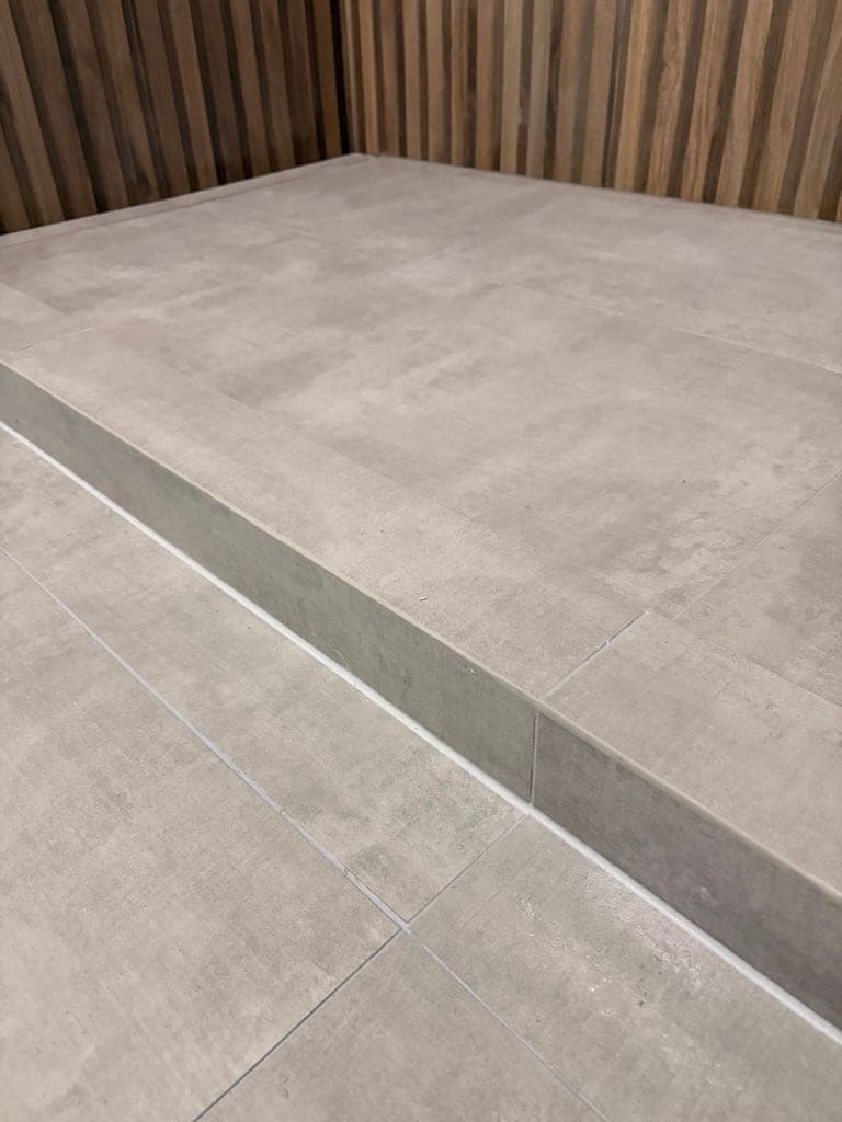 Shower floor and curb in concrete-look porcelain with a linear drain slot