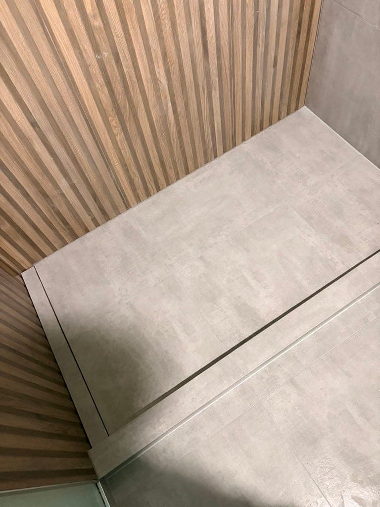 Concrete-look large-format shower floor meeting the slat tile wall