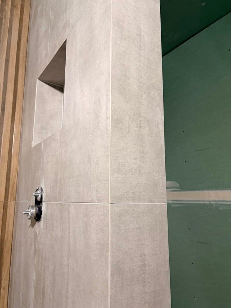 Concrete-look plumbing wall with a niche and valve rough-in, green board still exposed