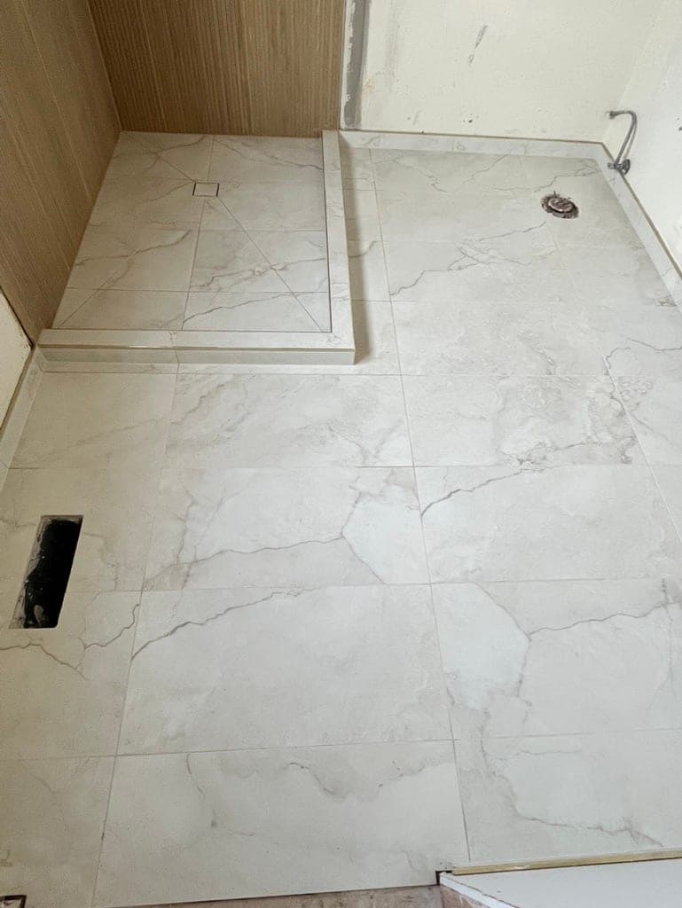 Bathroom floor in marble-look porcelain set up to the shower curb with the toilet flange still open
