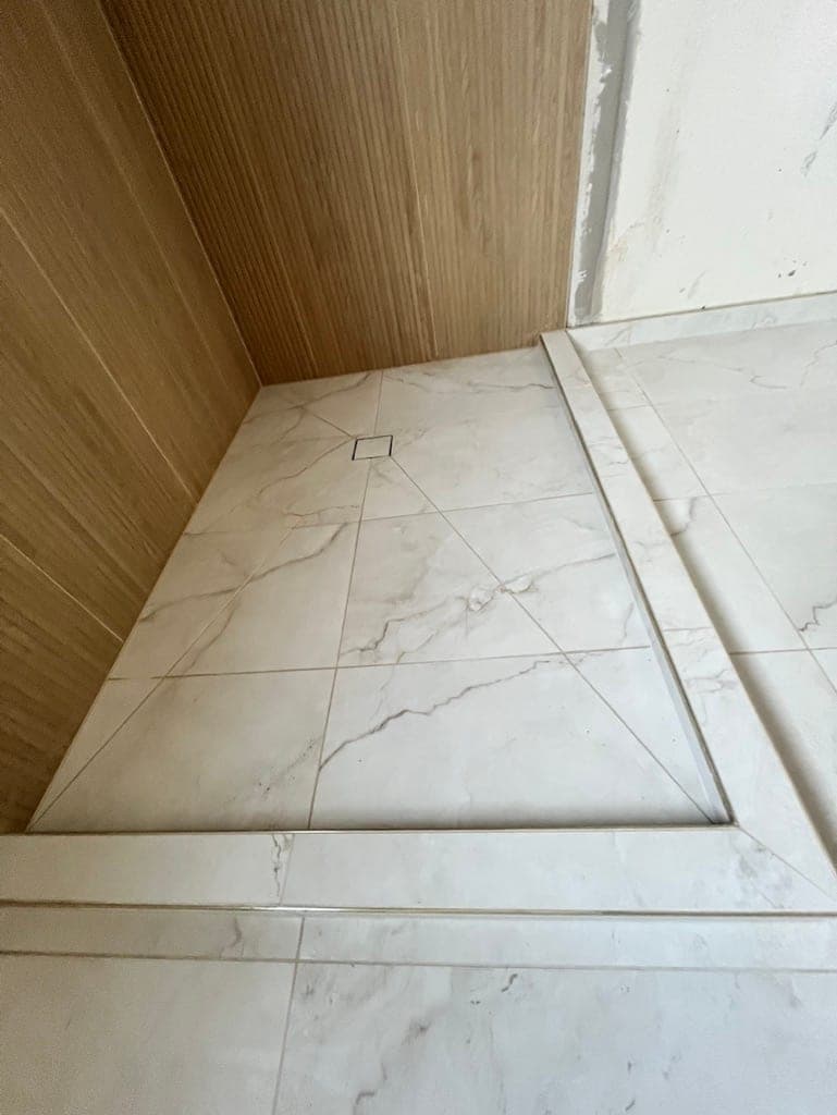 Marble-look shower floor with a square drain, pitched toward the drain, mid-install