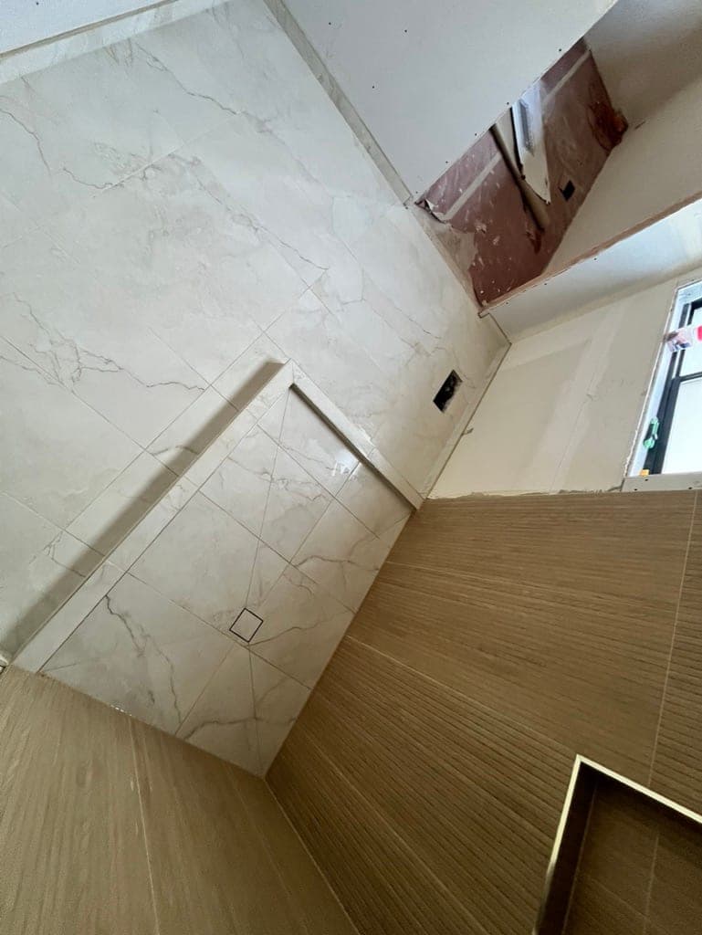 Marble-look wall panels meeting wood-look slat tile at the shower corner, mid-install