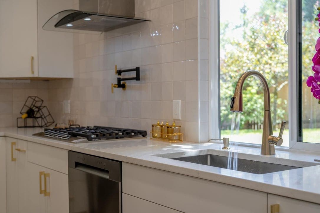 Cooktop with a black pot filler mounted in the glossy square tile backsplash