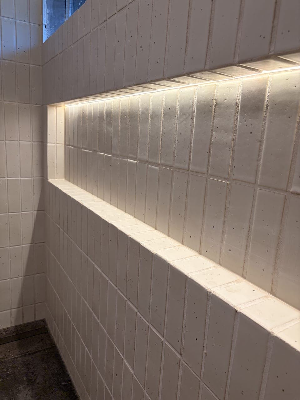 Close-up of the full-length shower niche lit by an LED strip in cream vertical-stack tile