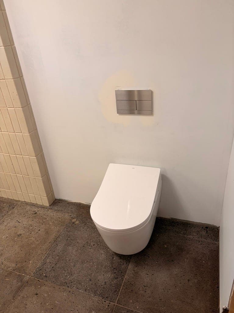 Wall-hung toilet on a dark stone-look floor next to the cream tile shower wall